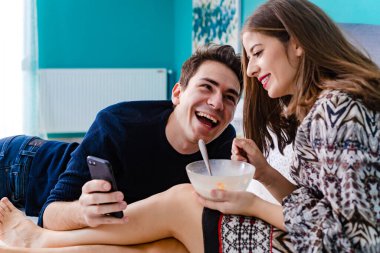 Erkek arkadaşı telefonunda kız arkadaşına bir şey gösteriyor. Gülümseyen, mutlu çift