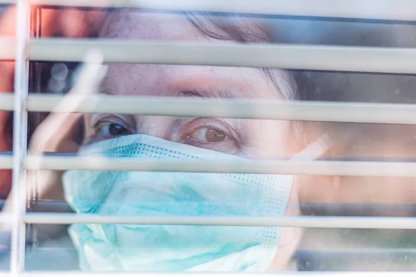 Фото Пожилой Женщины Медицинской Хирургической Маской Лице Заглядывающей Окно Изнутри — стоковое фото