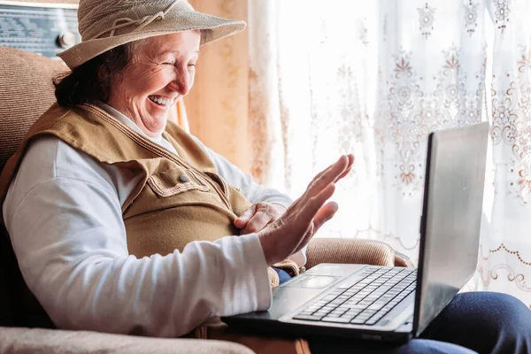 Yaşlı bir kadın ailesiyle görüntülü görüşme yapıyor, gülümsüyor ve el sallıyor. Karantina zamanı