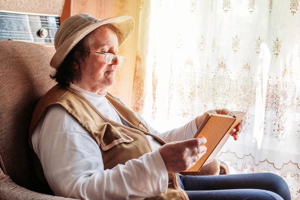 Starsza Kobieta Kapeluszu Czytająca Książkę Przy Oknie Światło Popołudniowe — Zdjęcie stockowe