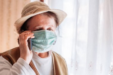 Tecritteki yaşlı kadın tıbbi maske takıyor, cep telefonuyla konuşuyor. Karantina hayatı
