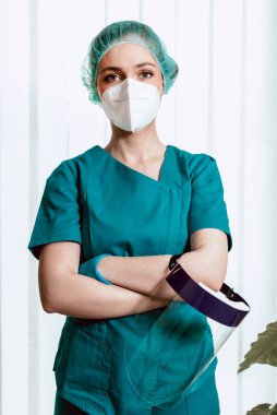 Nano maskeli, ameliyat üniformalı kadın doktor yüz kalkanı tutuyor, işe hazırlanıyor. Koronavirüs salgını