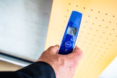 Normal vücut ısısını gösteren dijital temas olmayan termometreyi tutan adam.