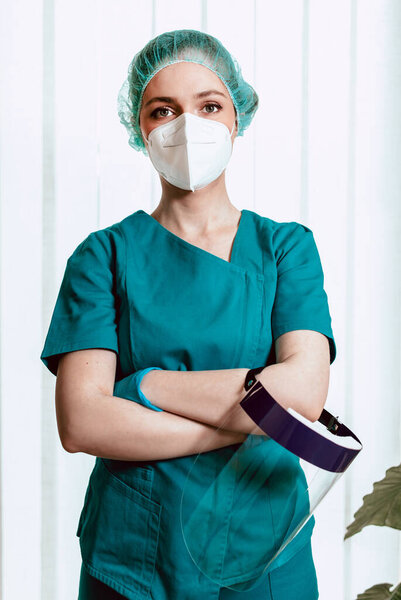 Женщина-врач в хирургической форме в наномаске держит щит для лица, готовится к работе. Пандемия коронавируса
