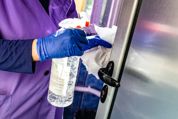 Temizlikçi kadın ofis binasında alkolle kapı kolunu temizliyor. Corona virüsü konsepti