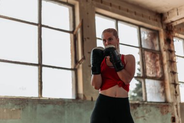 Boks antrenmanındaki sarışın güzel kız. Aktif yaşam tarzı. Pencerenin yanındaki eski binada çekilmiş. Boşluğu kopyala, yazmak için boşluk