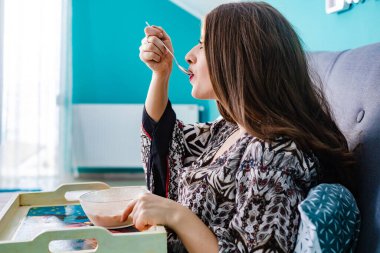 Genç, esmer kız sabahları mısır gevreği yiyor, yatakta.