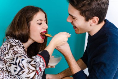 Birbirlerini besleyen mutlu genç çift. Erkek arkadaşı kız arkadaşını mısır gevreğiyle besliyor. Günaydın, kahvaltı zamanı.