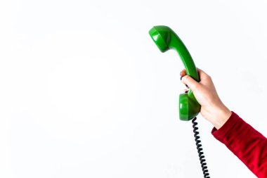 El ele tutuşup, beyaz arka planda izole edilmiş, bükülmüş kablosu asılı, eski yeşil telefon kulaklığı. Boşluğu kopyala, yazmak için boşluk