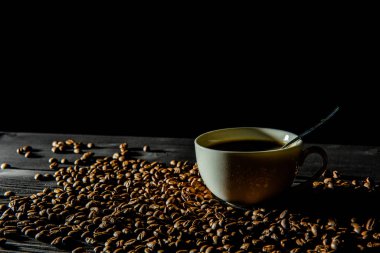 Siyah ahşap bir masada bir fincan kahve standı, kahve çekirdekleri etrafa saçılmış..