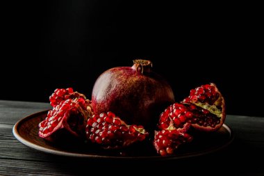 Koyu ahşap zemin üzerinde bir tabakta nar meyvesi.