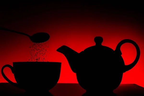 Kettle with a cup in red light, sugar poured from spoon into cup — Stock Photo, Image