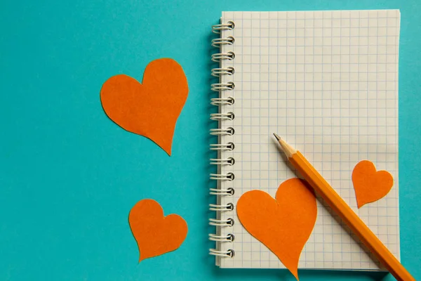 Bloc de notas, lápiz y corazones de color naranja sobre un fondo azul . — Foto de Stock