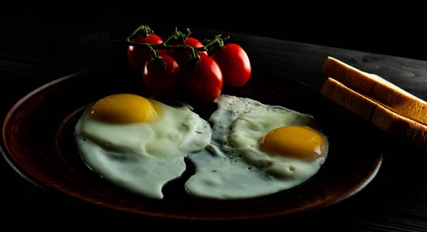 Café da manhã de ovos mexidos com tomates frescos e duas fatias de pão em um fundo escuro . — Fotografia de Stock