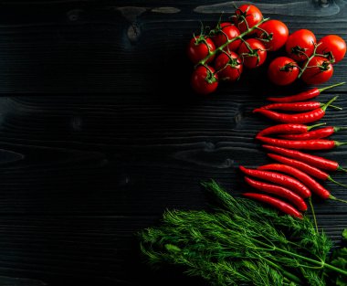 Siyah ahşap arka planda kiraz domatesleri, kırmızı biber ve taze otlar.