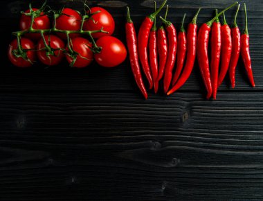 Siyah ahşap arka planda kiraz domatesleri ve kırmızı biber.