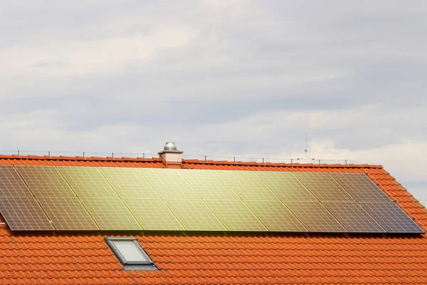 Photovoltaic or solar panels on roof of the house at sunset. Red roof with ecological solar system during the summer day. Clouds in the background.