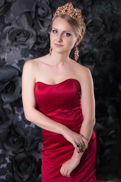 Beautiful young blonde woman in red long dress with fluffy skirt on a black background. queen, golden crown on the head, golden curls, passionate girl in red — Stockfoto