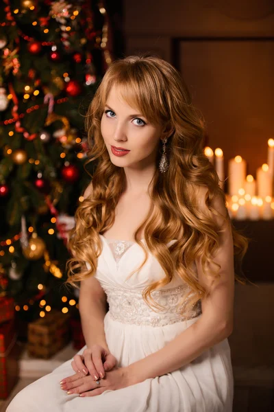 Молодая красивая блондинка в белом платье на Рождество, женщина в красивой комнате с елкой и свечами, девушка с подарками, золотые волосы, счастливая женщина Новый год, рыжая девушка улыбается — стоковое фото