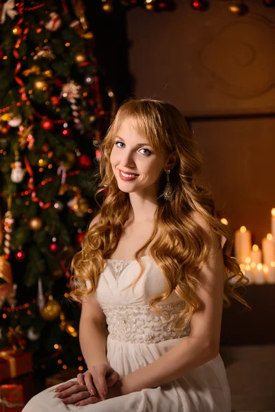 Young beautiful blond woman in the white dress on christmas, woman in a beautiful room with a Christmas tree and candles, a girl with gifts,  golden hair, happy woman new year, Redhead girl smiling — ストック写真