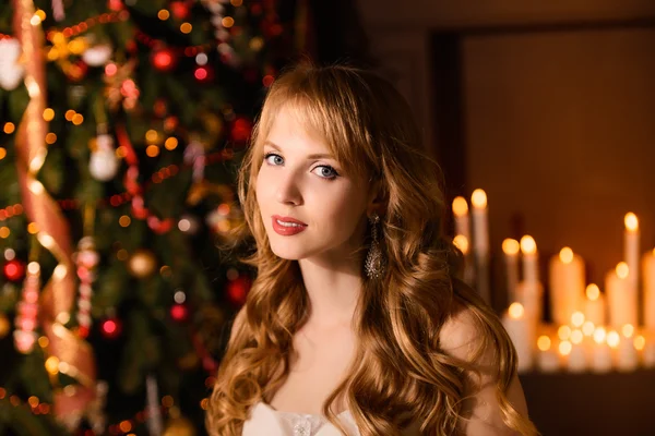 Young beautiful blond woman in the white dress on christmas, woman in a beautiful room with a Christmas tree and candles, a girl with gifts,  golden hair, happy woman new year, Redhead girl smiling — Stock fotografie