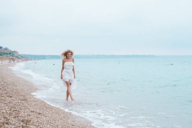 , bir mayo, kot şort, mutlu bir kadın, sahilde, neşeli kız seksi, ayaklarda su dalgalar üzerinde yürüme gülümseyen kadın sahilde, yürüyen güzel genç kadın