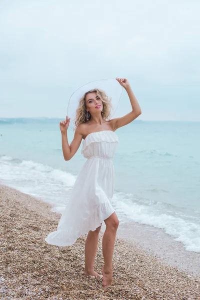 Schöne junge Frau am Strand, lächelnd, im Badeanzug, in Jeanshosen, eine glückliche Frau, fröhliches Mädchen am Strand, sexy Frau, Füße im Wasser, auf den Wellen gehen Stockbild