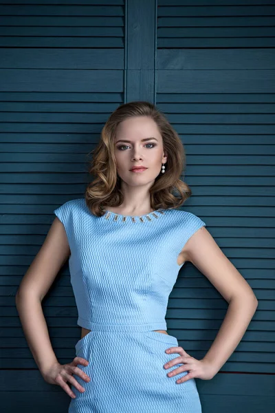 Schöne junge blonde Frau auf blauem Hintergrund, reiche glamouröse Frau in einem blauen Abendkleid sucht direkt Stockbild