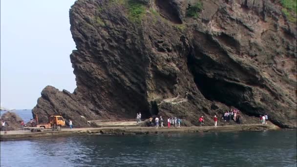 Pessoas andando debaixo da rocha na costa — Vídeo de Stock