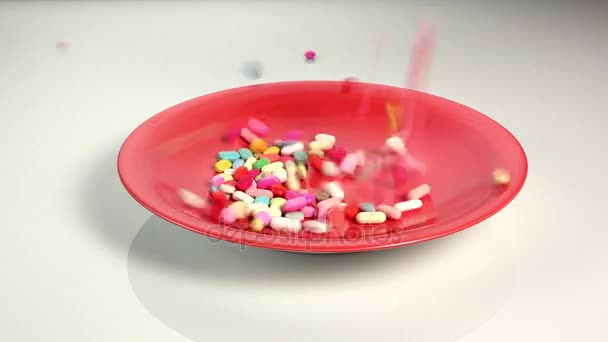 Píldoras de colores cayendo en plato rojo — Vídeos de Stock