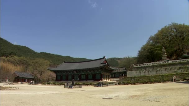 背景の山と木韓国における伝統的な寺院建築の領土の上を歩く人 — ストック動画