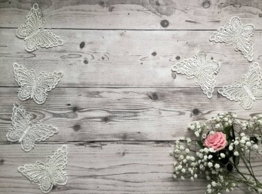Hafif ahşap arka planda düz bir konsept, küçük beyaz çiçekler ve beyaz tekstil kelebekleriyle birlikte pembe bir gül.