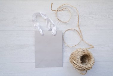 Açık gri arka planda düz bir yaşam fikri, gri bir kağıt hediye çantası ve jüt halat makarası