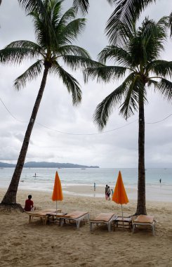 Boracay, Filipinler - 17 Aralık 2015. Yağmurlu gün Boracay, Filipinler, beyaz plajda palmiye ağaçları ile rahatlatıcı sandalye.