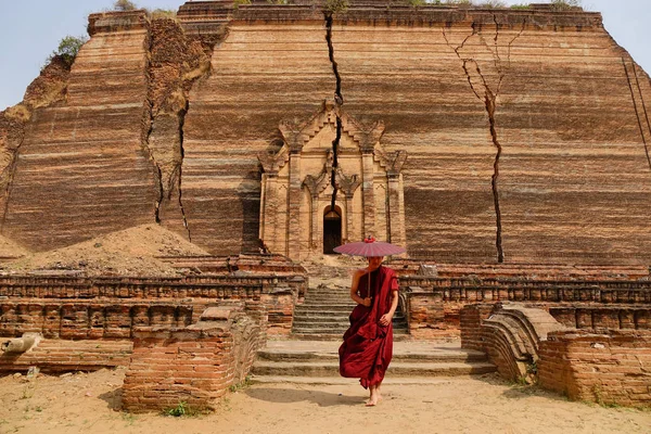 A Buddhist monk in the red robe with umbrella at the acient pagoda in Myanmar.