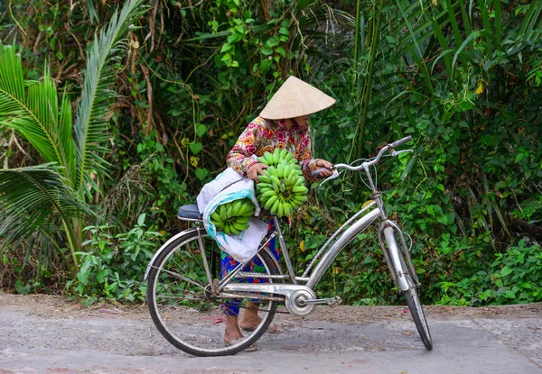 Μια γριά γυναίκα κουβαλάει μπανάνα δίπλα στο ποδήλατό της. — Φωτογραφία Αρχείου