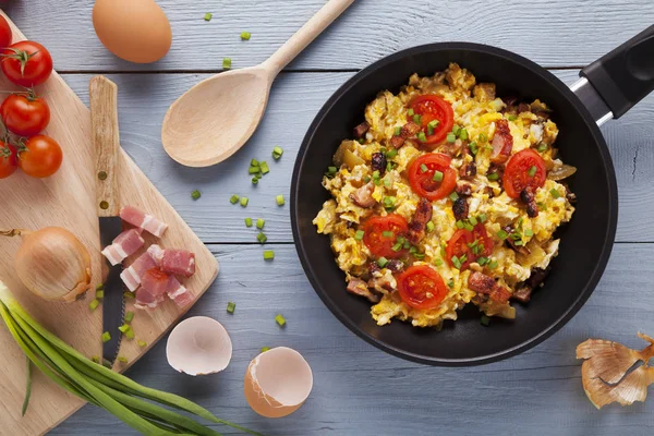 Scrambled eggs in a pan with bacon, onion and tomatoes sprinkled — Stock Photo, Image