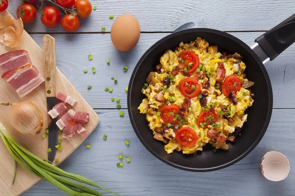 Scrambled eggs in a pan with bacon, onion and tomatoes sprinkled — Stock Photo, Image