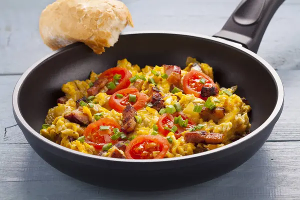 Scrambled eggs in a pan with bacon, onion and tomatoes sprinkled — Stock Photo, Image