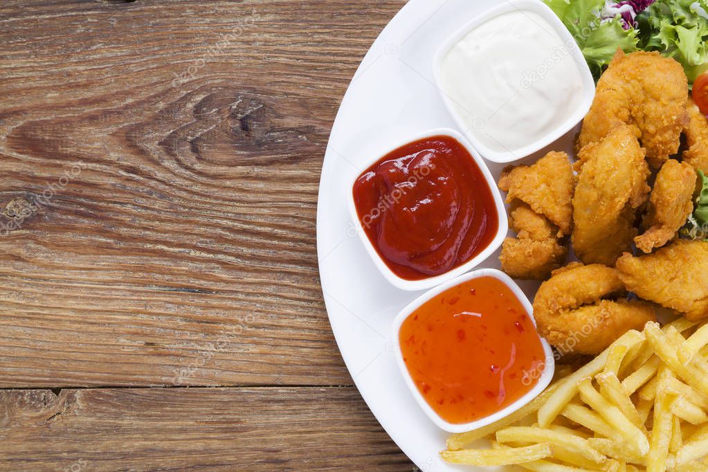 Nuggets and chips on a plate served with dip and salads 