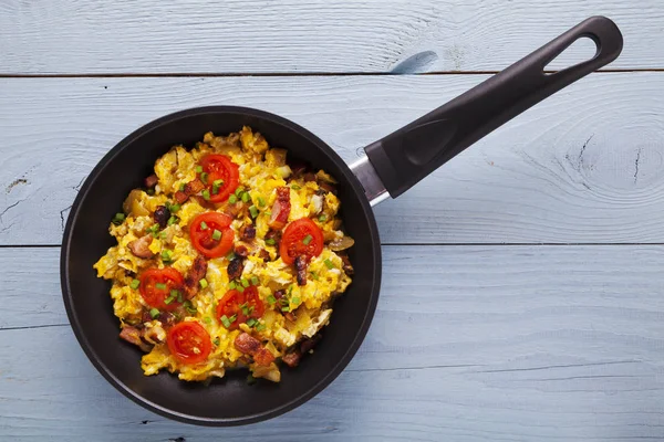 Roerei in een pan met spek, ui en tomaten besprenkeld — Stockfoto