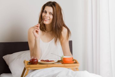 Genç bir kadın otel yatağında kahvaltı yapıyor..