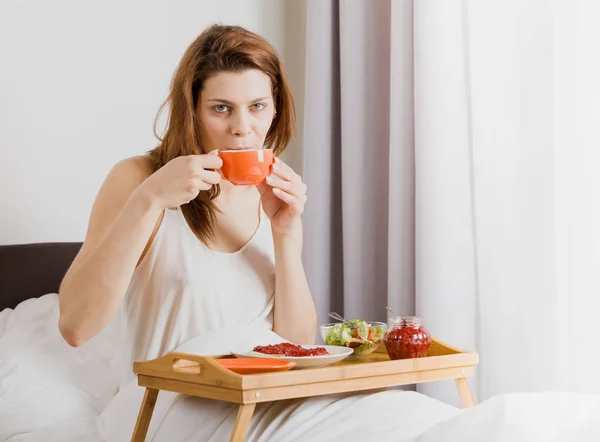 Giovane donna che fa colazione nel letto dell'hotel . — Foto Stock