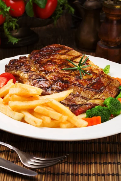 Grilled beef steak served with French fries and vegetables on a — Stock Photo, Image