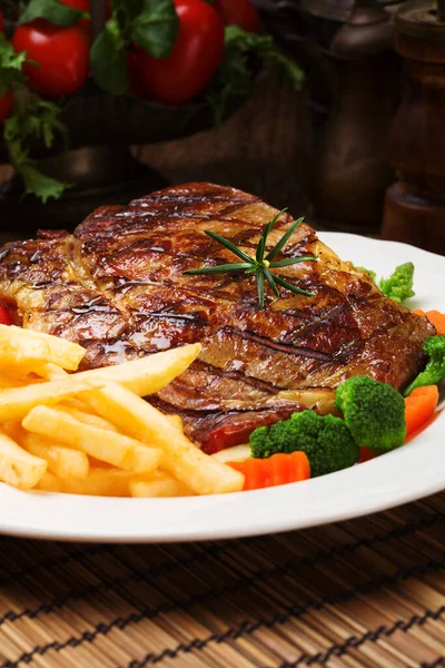 Grilled beef steak served with French fries and vegetables on a — Stock Photo, Image