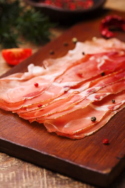 Delicious prosciutto ham on a wooden board with spices. — Stock Photo, Image