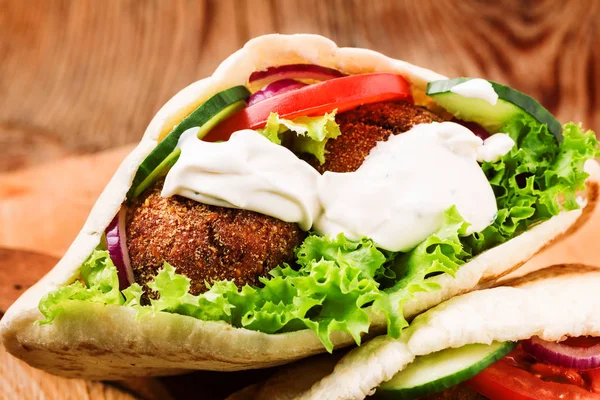 Falafel i świeże warzywa w chlebie pita na drewnianym stole — Zdjęcie stockowe