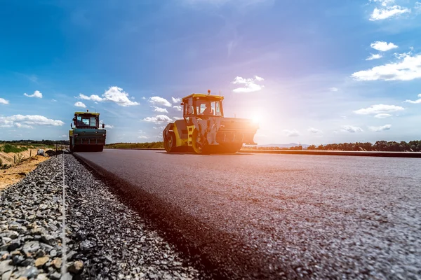 Puesta de sol sobre el rodillo de carretera trabajando en el sitio de construcción — Foto de Stock