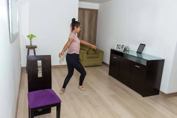 Genç kız, bale, dans ve jimnastik yapıyor. Oturma odasında tabletinden internet dersini izliyor.