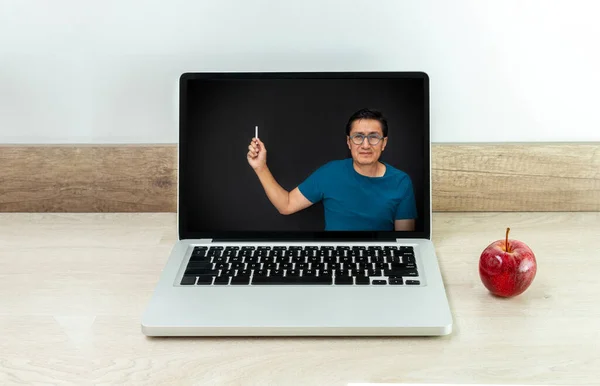 Laptop with a teacher teaching online classes on the internet on a black board due to coronavirus. The laptop is on a desk with an apple next to it